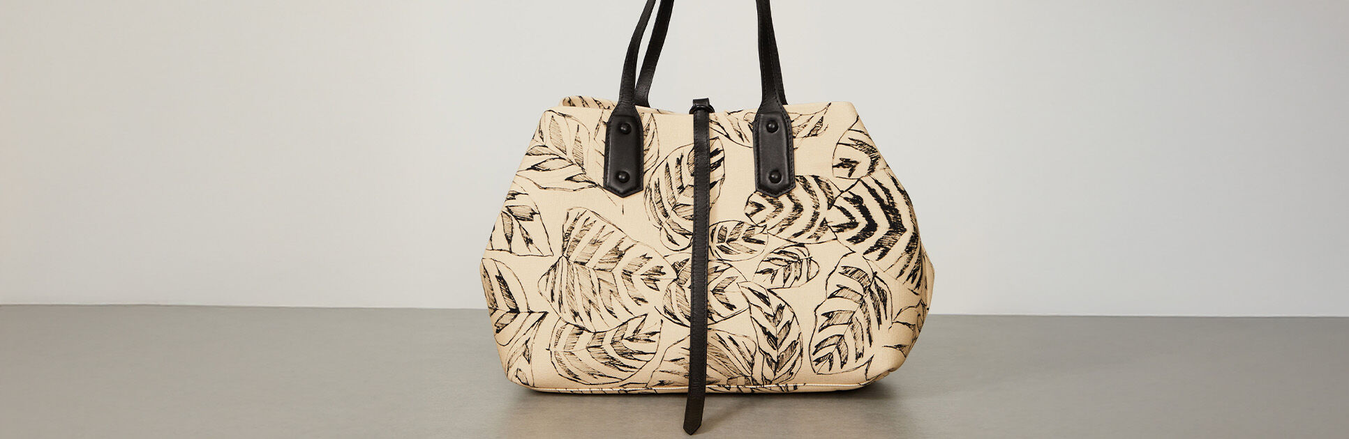 Bolsa com estampa de folhas verdes em fundo claro.