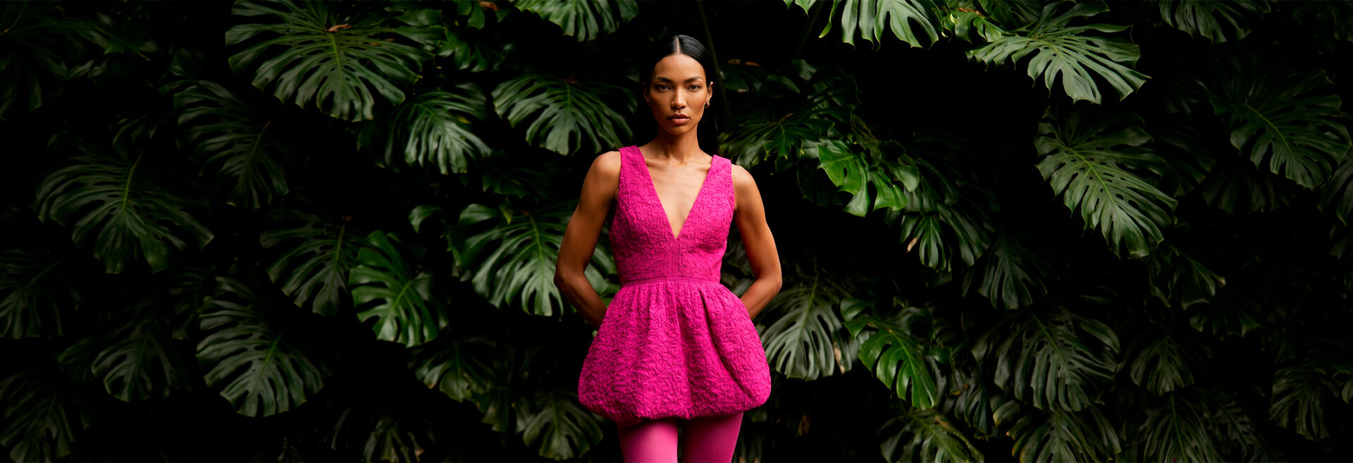 Modelo com vestido rosa em fundo verde tropical.